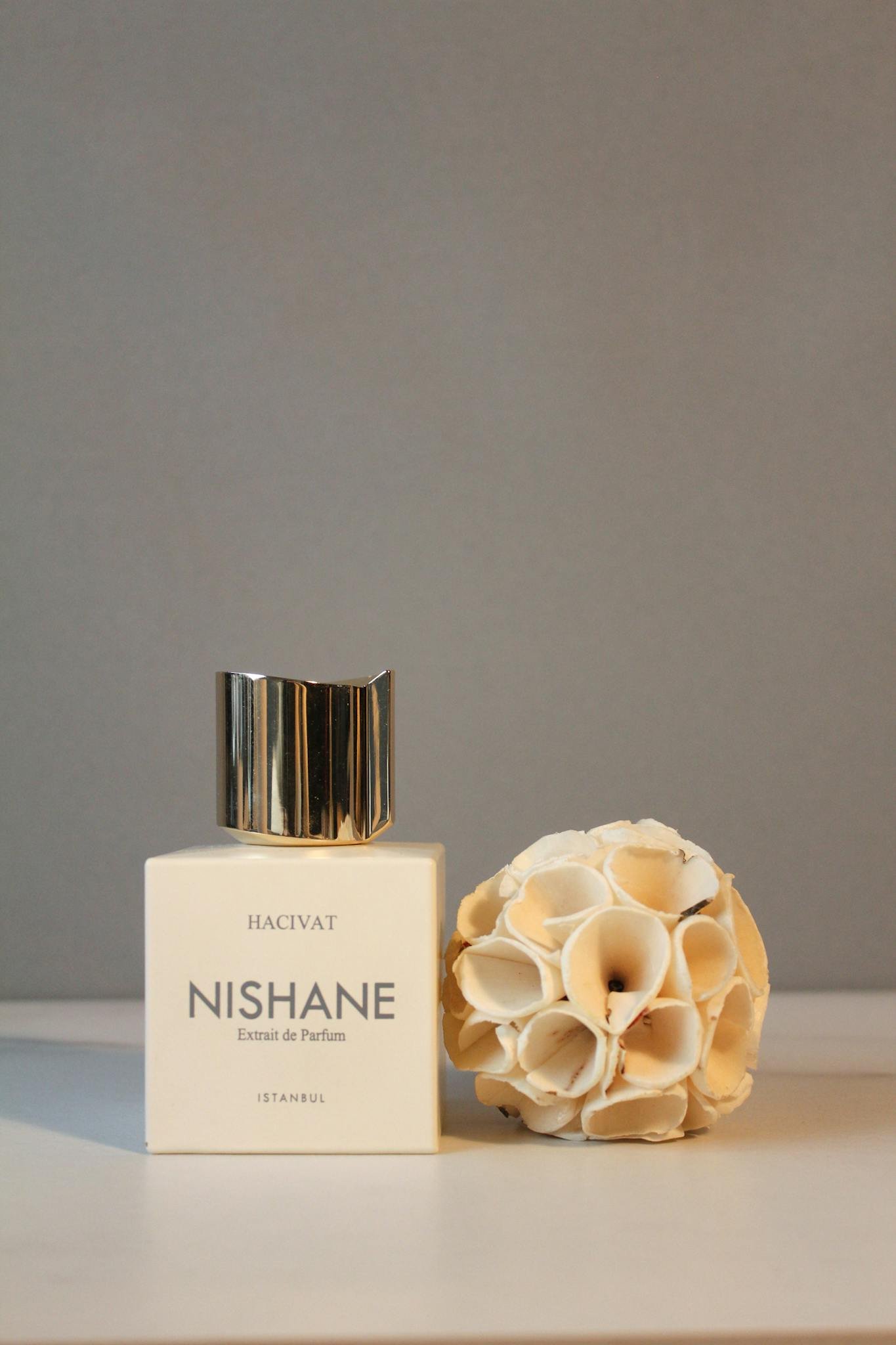 Elegant display of Nishane perfume bottle with decorative dried lotus against minimalist background.